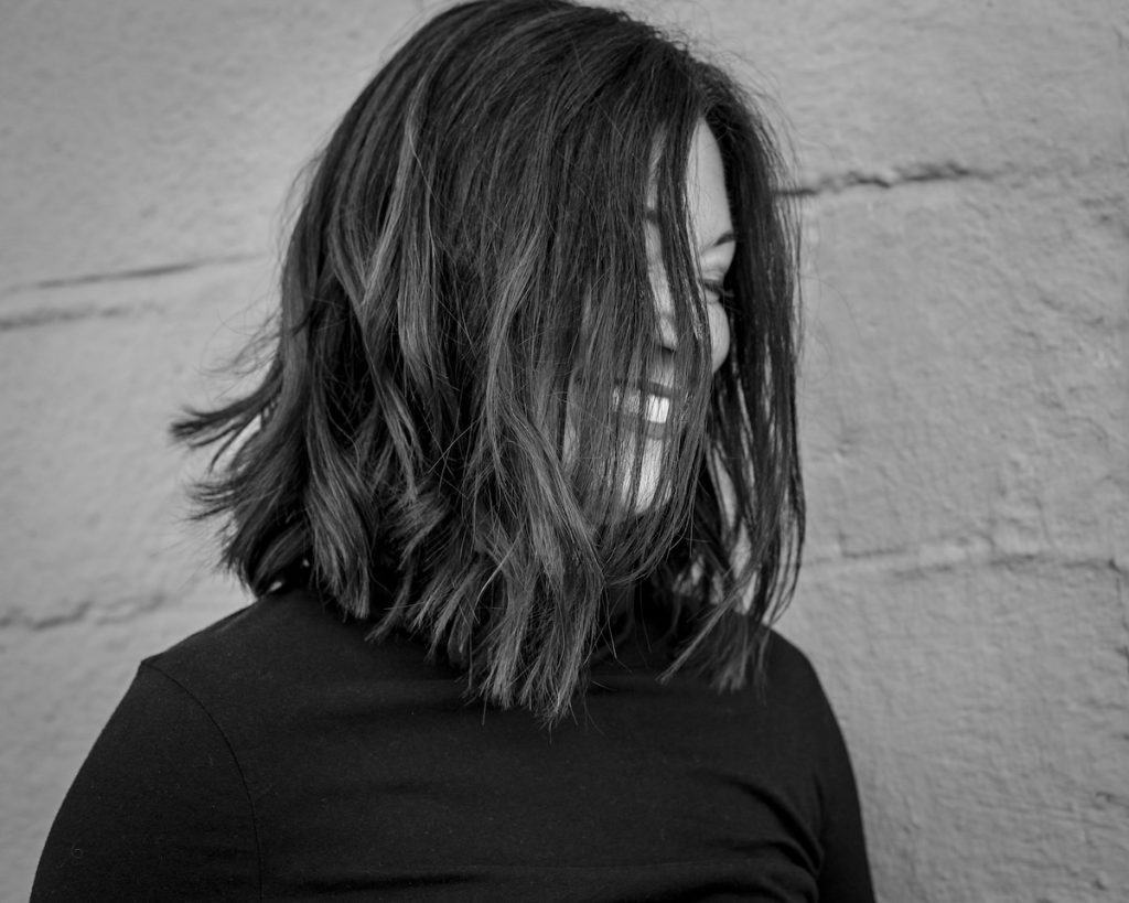 woman in a black shirt laughing with hair cover her face
